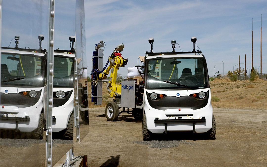 The ICARUS prototype vehicle and robotic arm beside mirrored heliostats at a solar field.