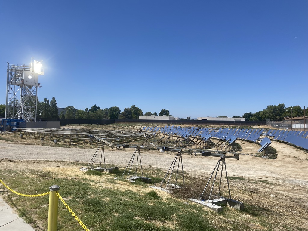 Rows of heliostats in a solar test field with an illuminated receiver tower on the left.